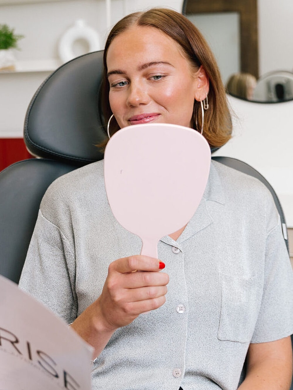 Woman admiring reflection in pink hand mirror.